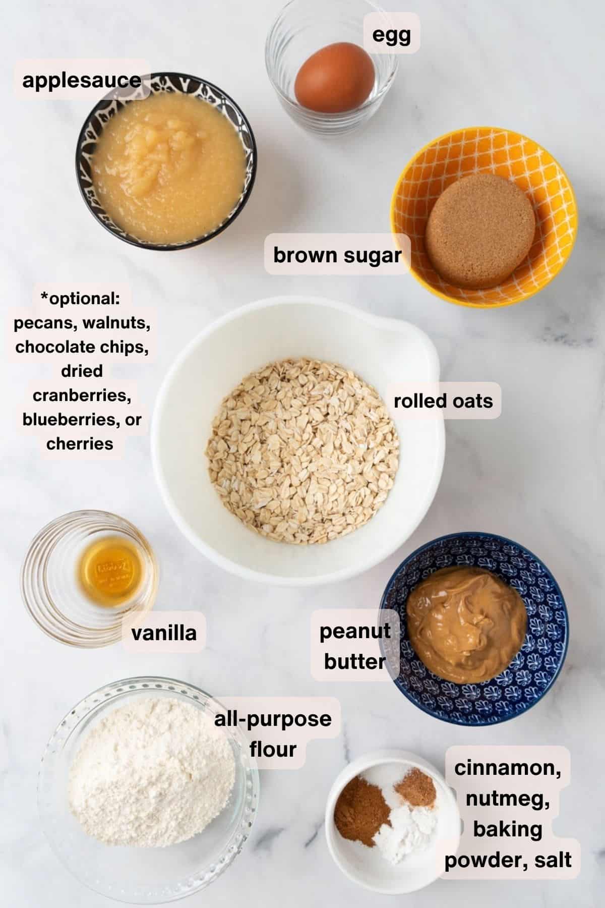 Ingredients for applesauce oatmeal breakfast bars in various bowl on a white marble counterop.