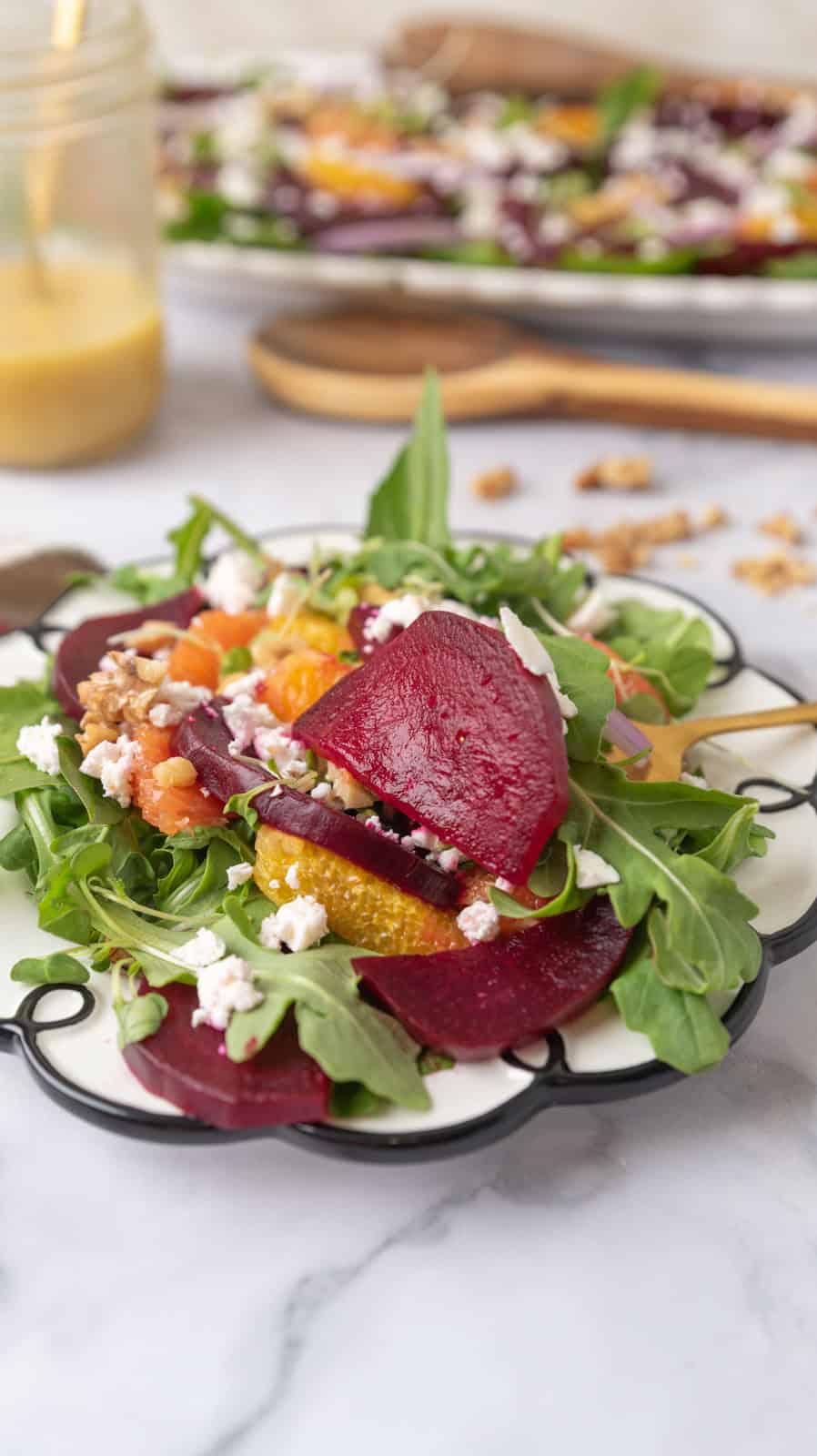A closeup of a salad plate filled with beet and citrus salad, a fork inserted into the salad. The plate has a whimsical swirl around the edge.