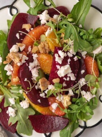 A bright and colorful beet and citrus salad piled onto a whimsical whait plate with black swirls around the edge.