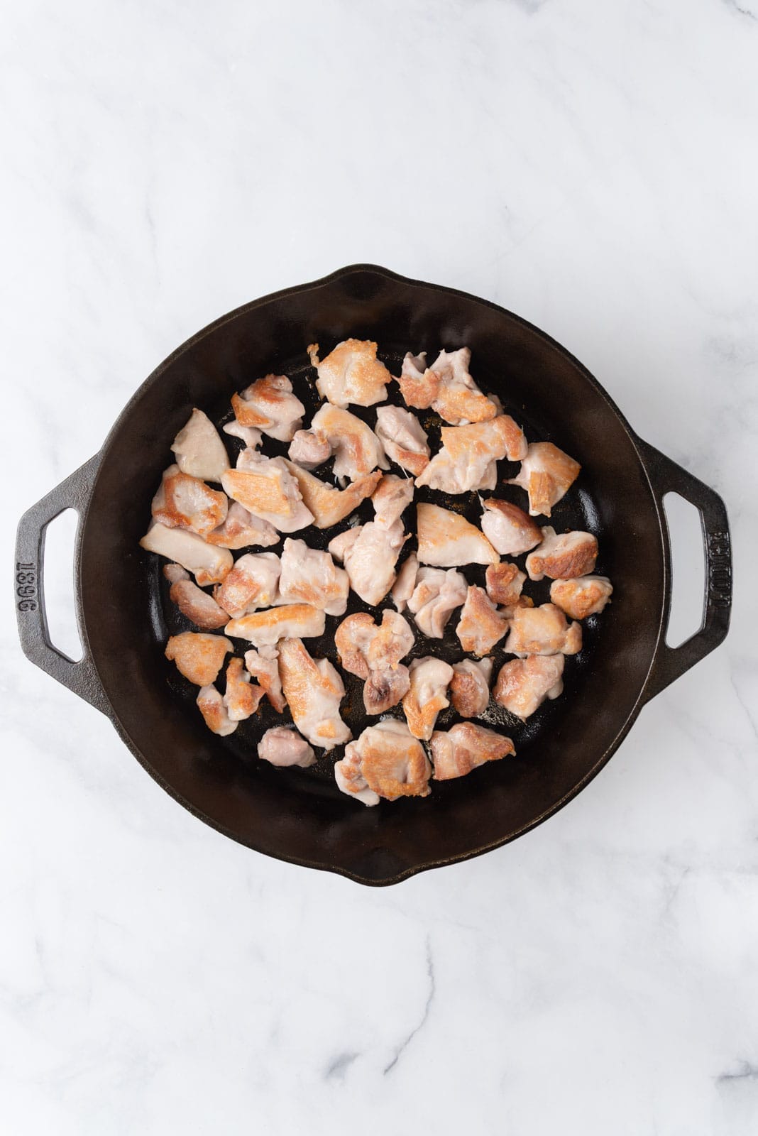 A cast iron skillet with browned chunks of boneless skinless chicken thighs.
