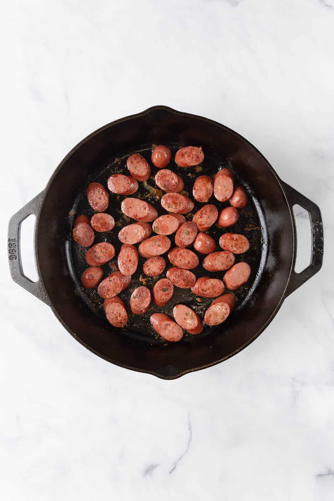 A large cast iron skillet with browned chicken sausage slices.