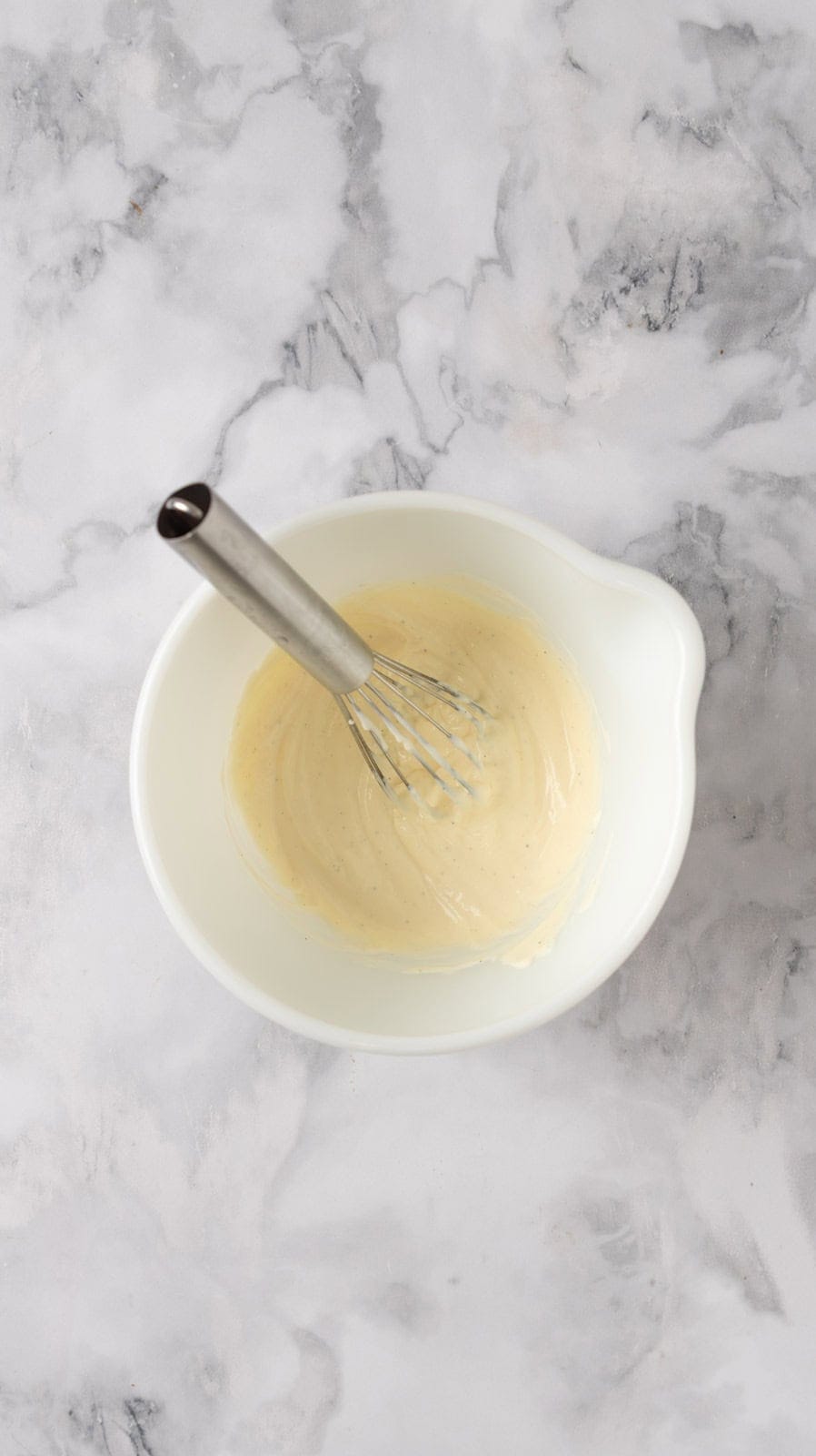 Dressing for chicken salad mixed together in white mixing bowl with a small whisk still in the bowl.