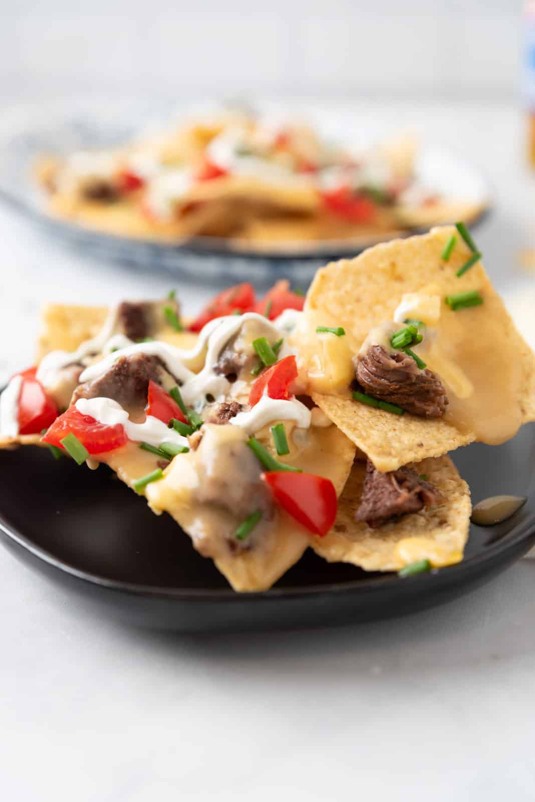 A small black appetizer plate filled with colorful nachos.