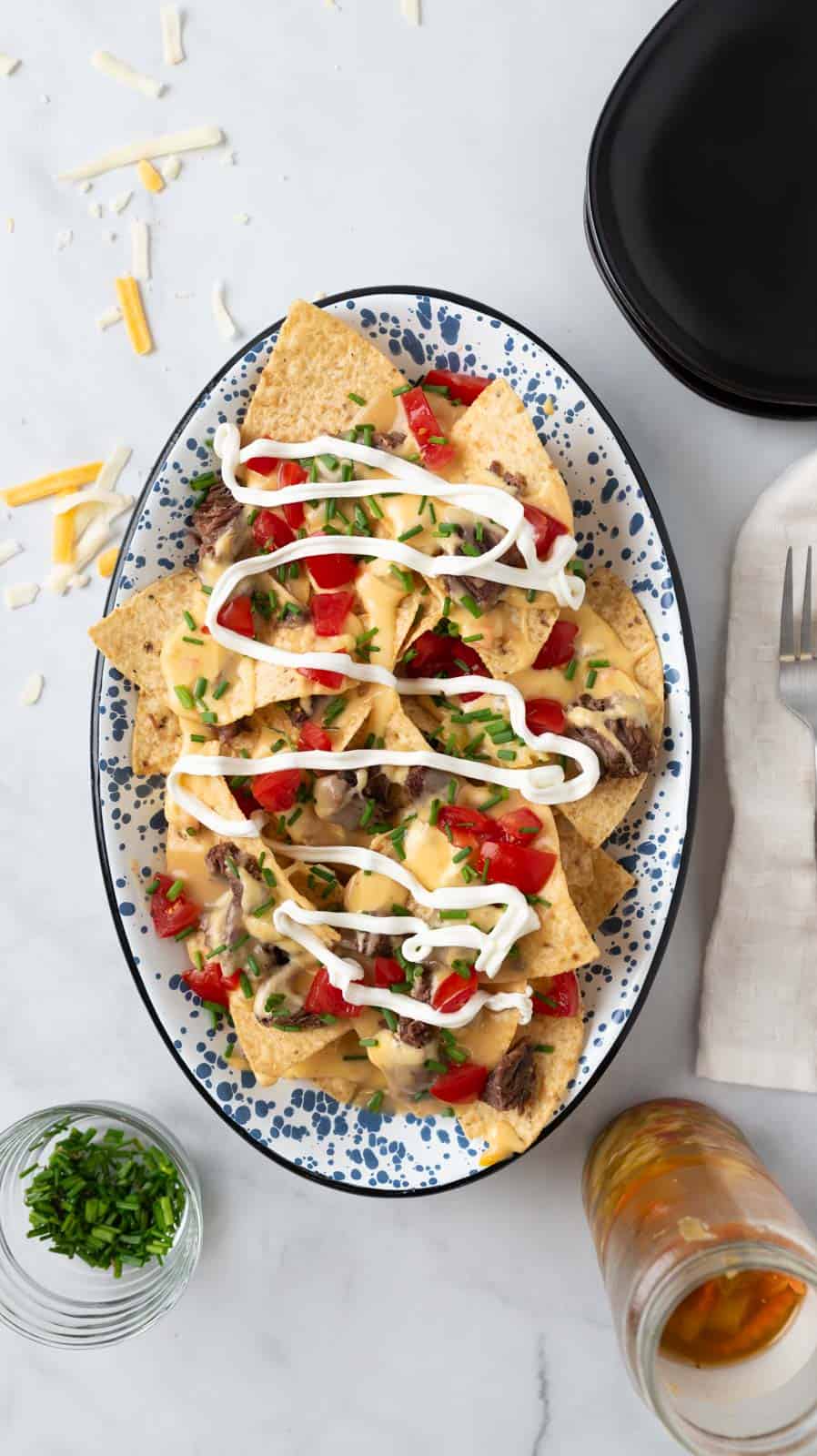 A garnished platter of pot roast nachos sitting on a white marble countertop with garnishes scattered around the frame.