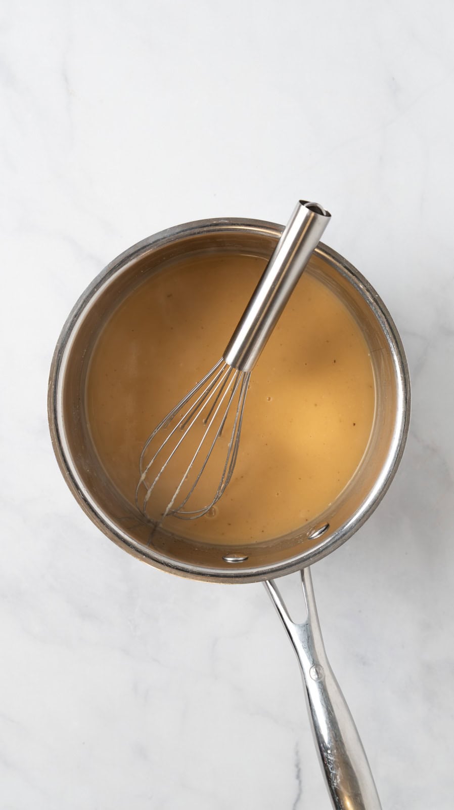 Pot roast gravy in a small saucepan resting on a white marble countertop.
