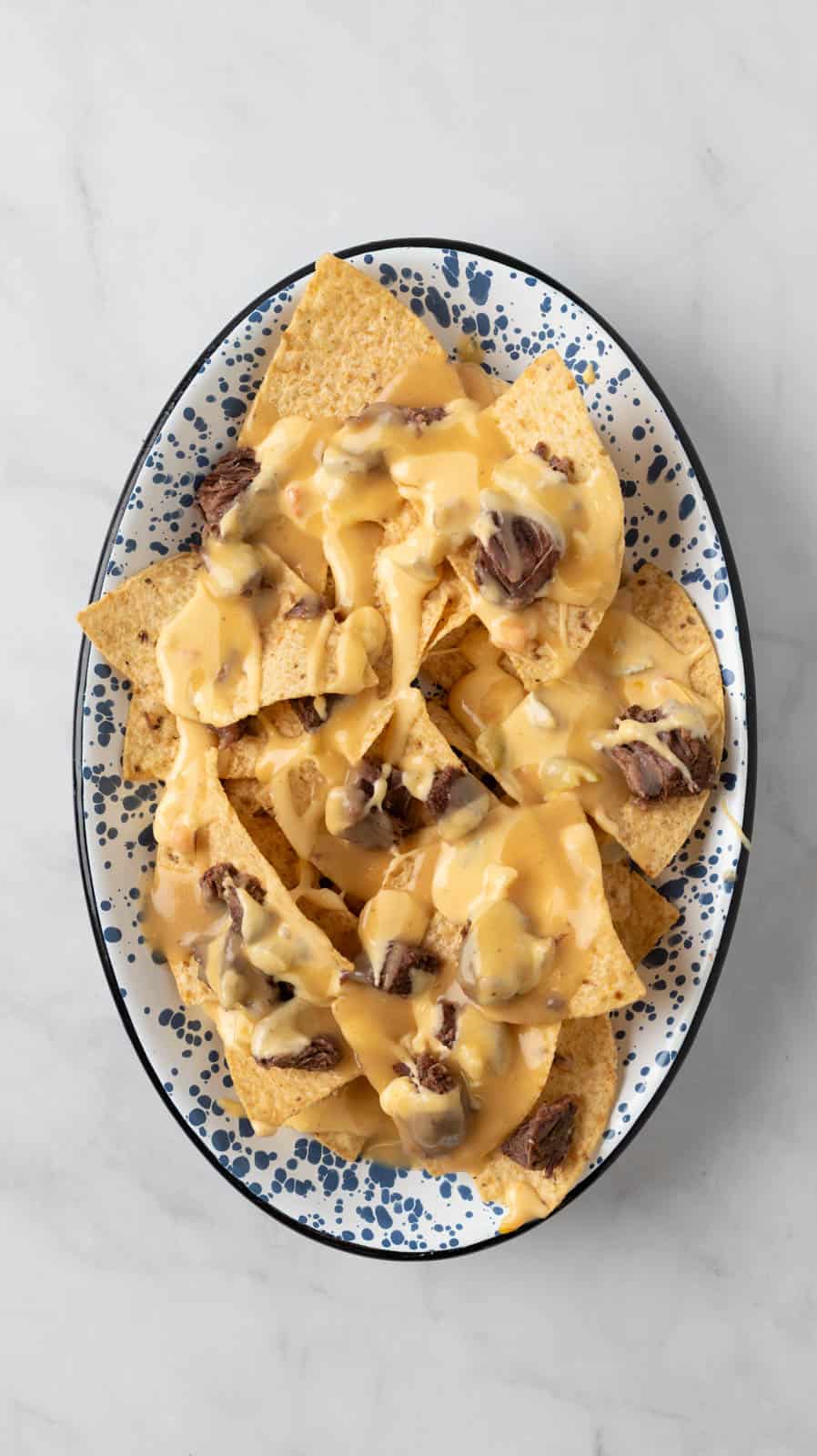 Layering tortilla chips, pot roast bites, gravy and cheese sauce on a nacho platter.