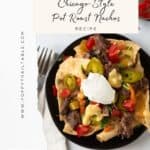 A close-up of a small black plate loaded with cheesy nachos sitting on a white marble coutnertop with a napkin and fork beside the plate. Avocados and toamtoes near the plate.